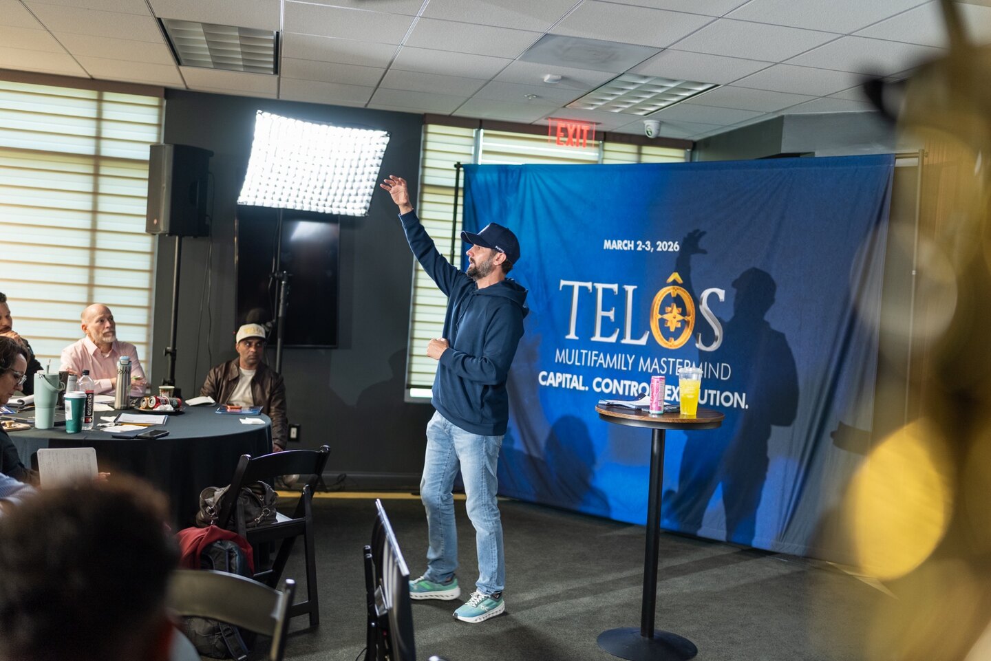 A speaker presenting in front of the March 2026 TELŌS backdrop